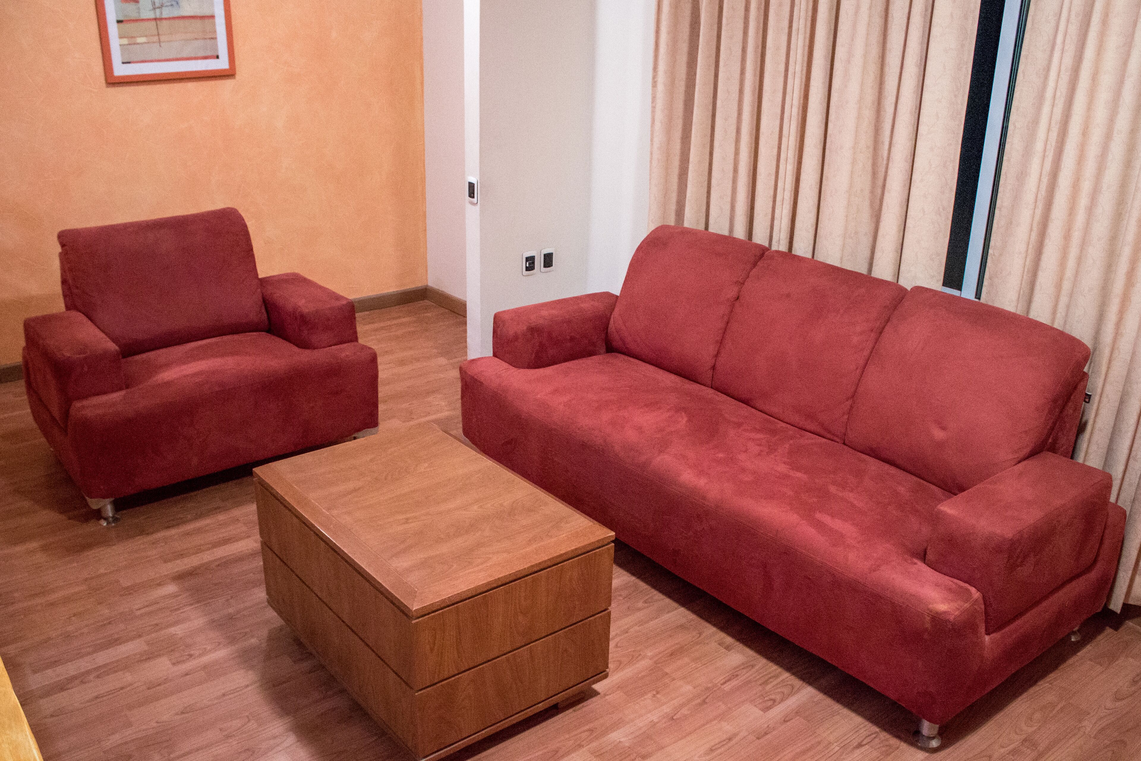Une pièce avec un canapé rouge, un fauteuil assorti et une petite table en bois.