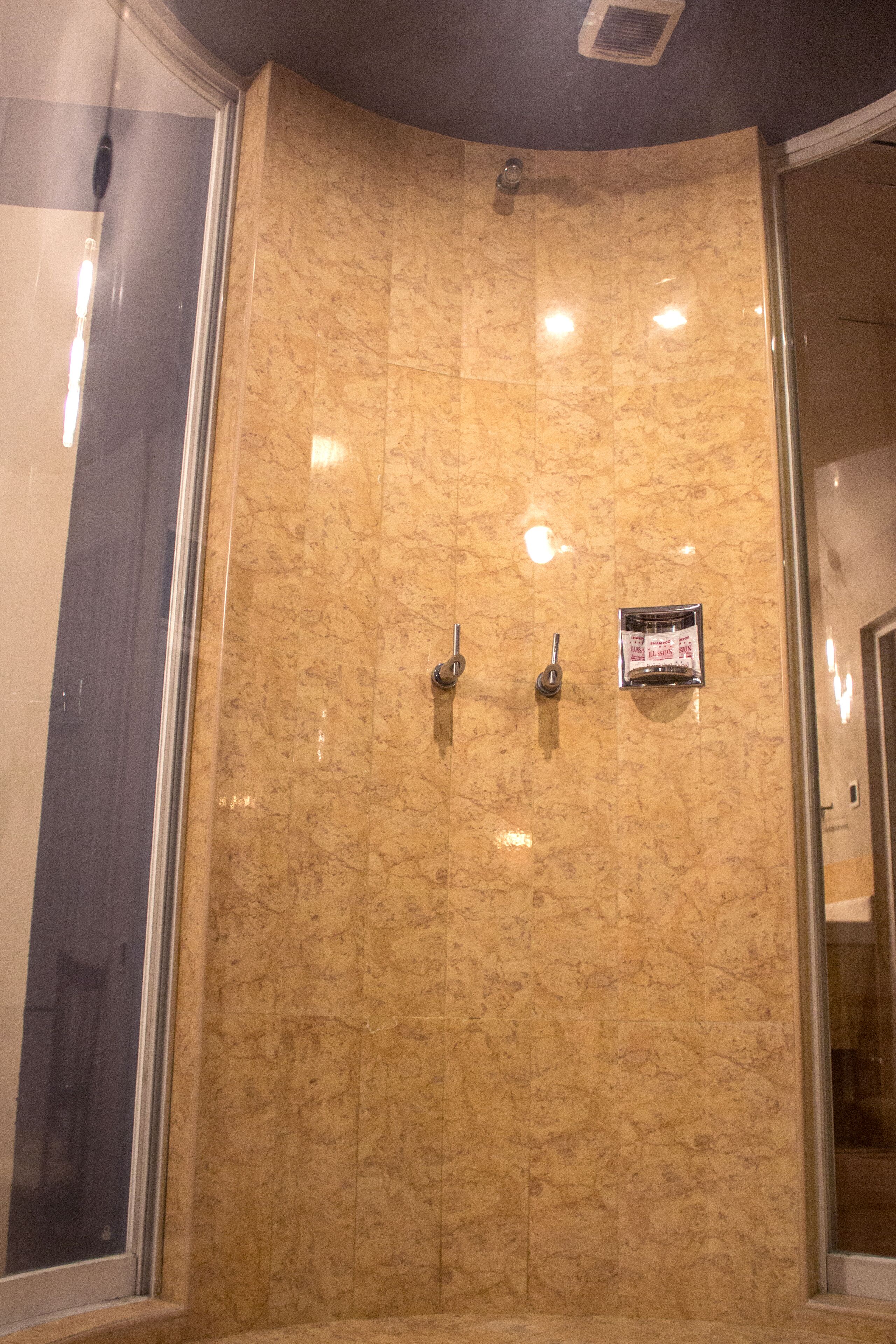 A shower area with a marble wall, a glass door, and a small sign on the wall.