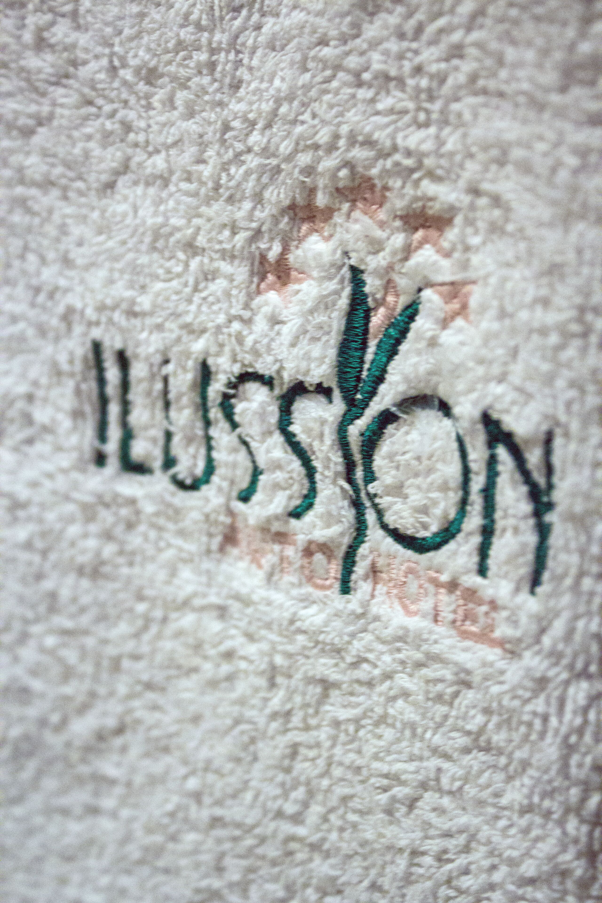 Detailaufnahme eines strukturierten Stoffes, mit dem Wort "ILLUSION" in grün bestickt.