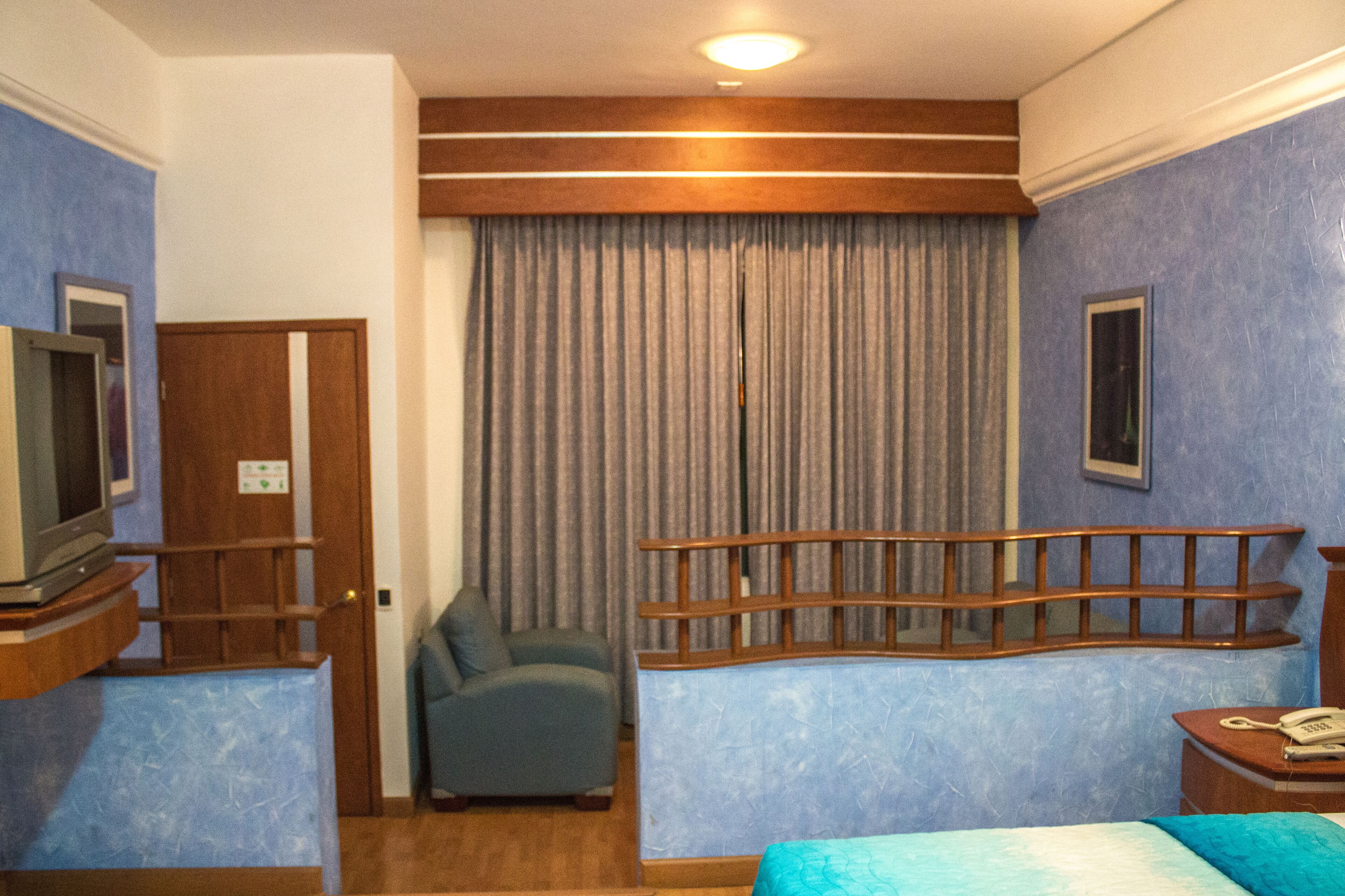 A hotel room with a bed, a chair, a television, a telephone, and a curtain.