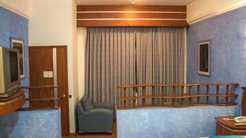 A hotel room with a bed, a chair, a television, a telephone, and a curtain.
