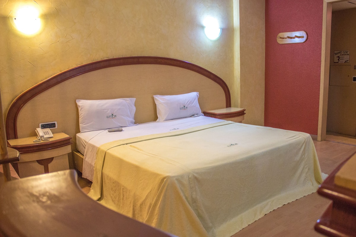 A hotel room with a single bed, a bedside table with a phone, and a nightstand.