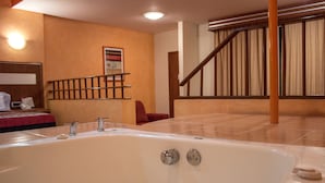Un baño moderno con una bañera grande, ducha y retrete. Se ve una escalera de madera que sube a otro nivel.