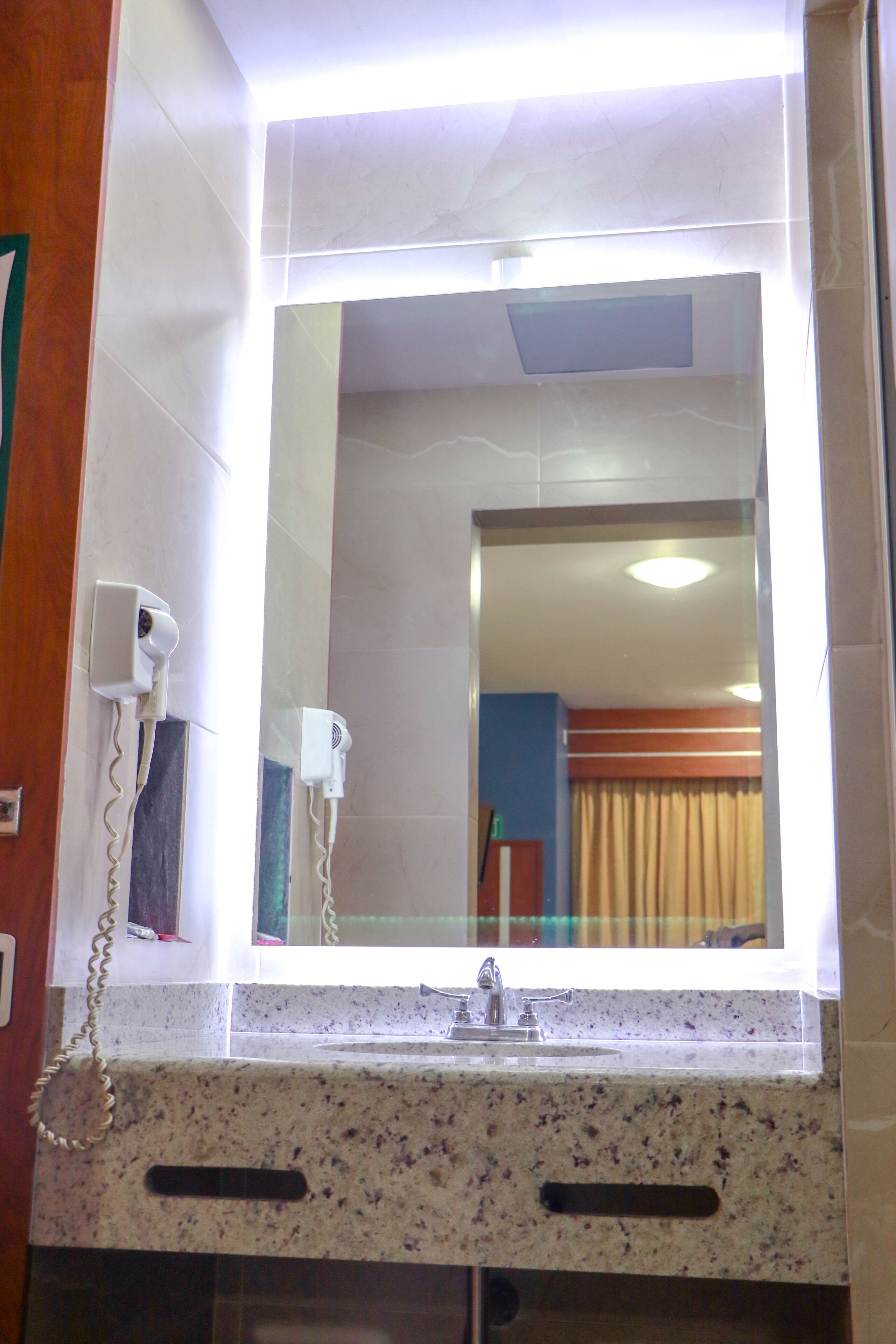 Un baño con espejo, secador de pelo y lavamanos.