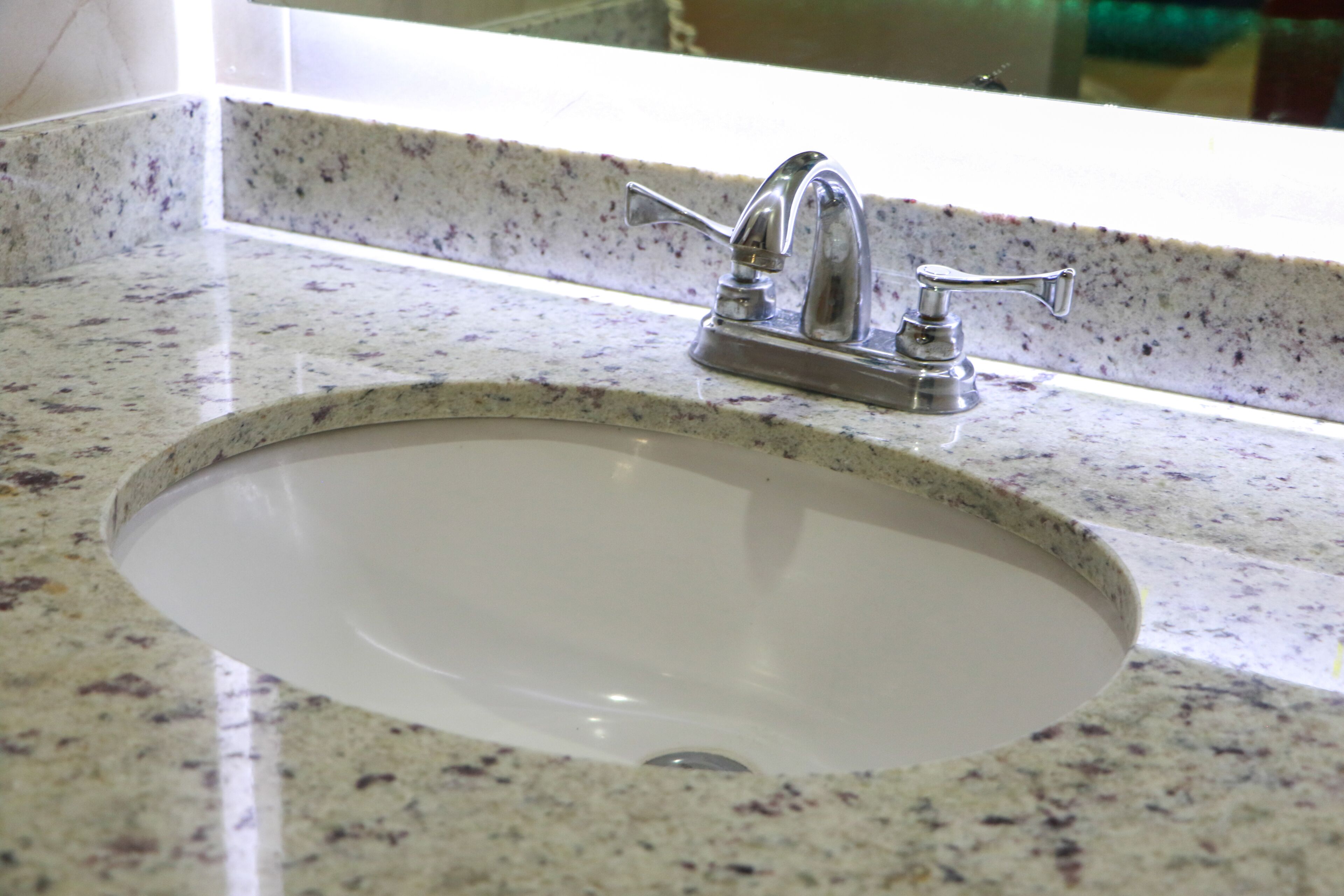 A bathroom sink with a granite countertop and a chrome faucet.