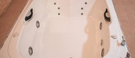 A white bathtub with multiple faucets and a drain.