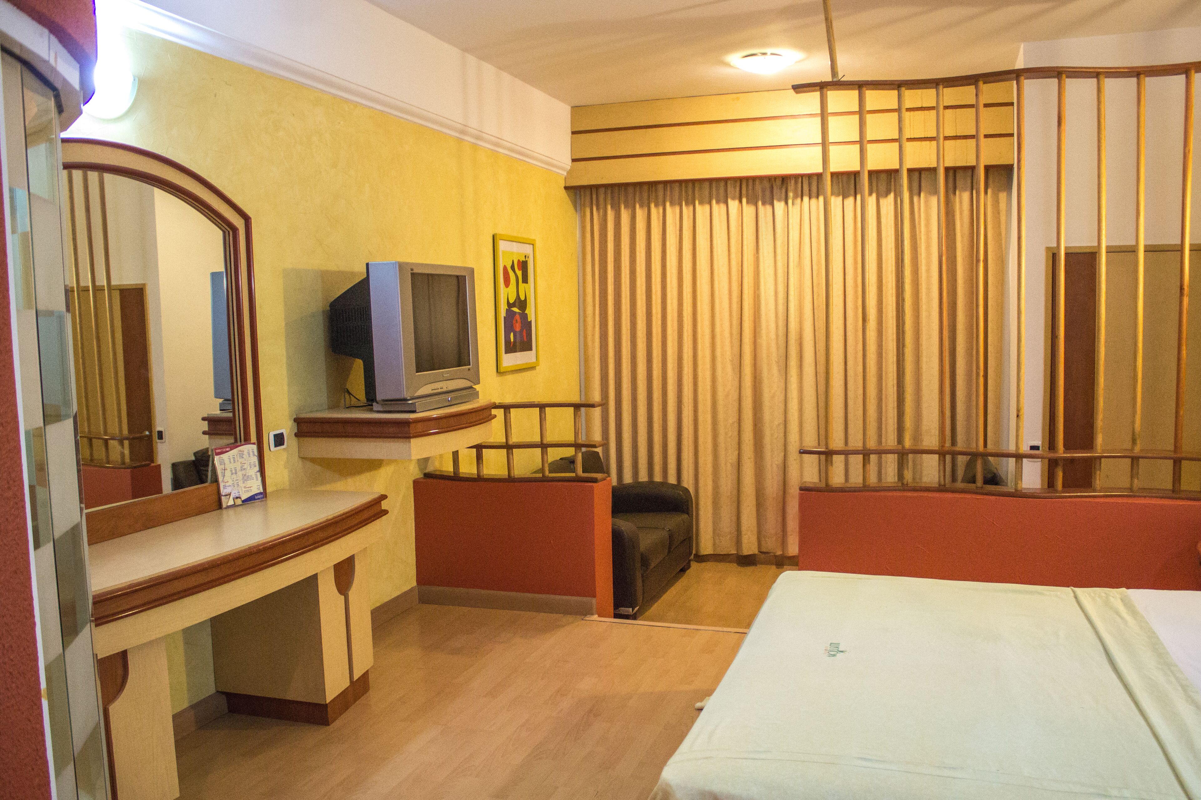 Habitación de hotel con cama, escritorio con televisor, espejo y ventana con cortinas.