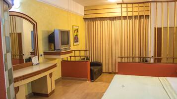 Habitación de hotel con cama, escritorio con televisor, espejo y ventana con cortinas.