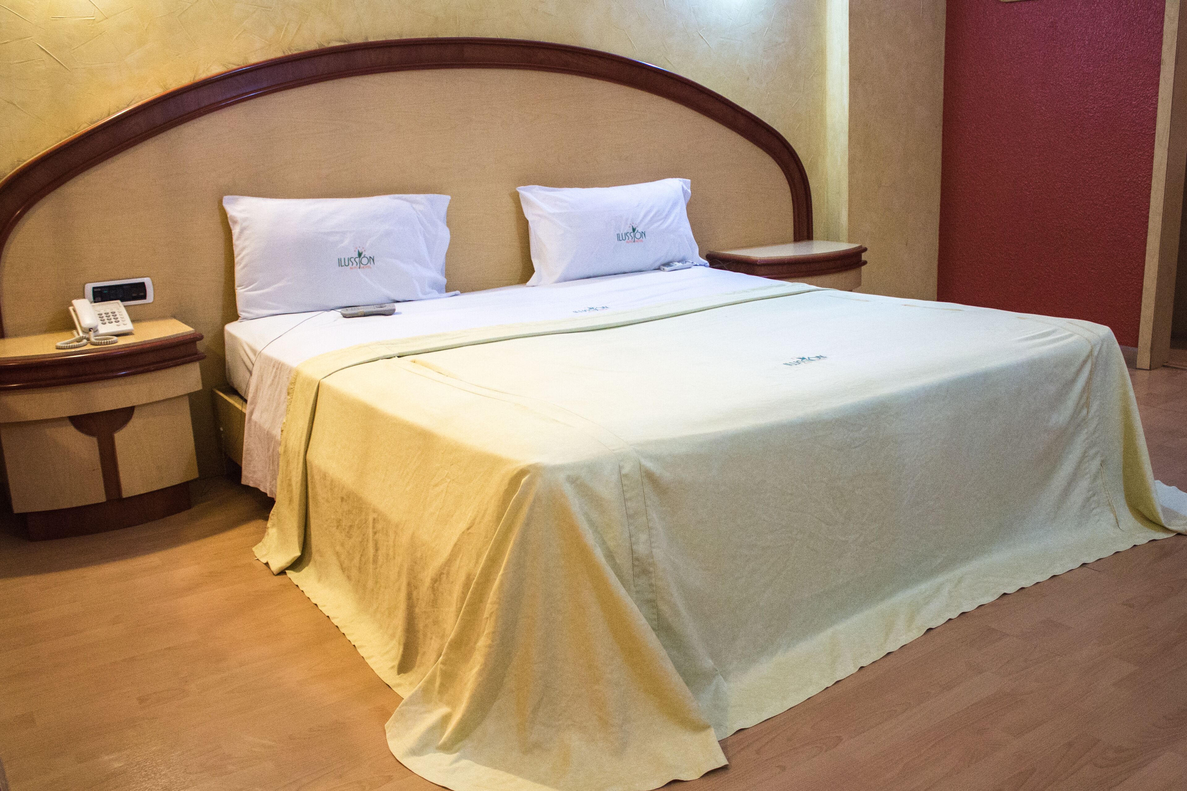 A hotel room with a large bed, two pillows, a bedside table with a phone, and a nightstand.