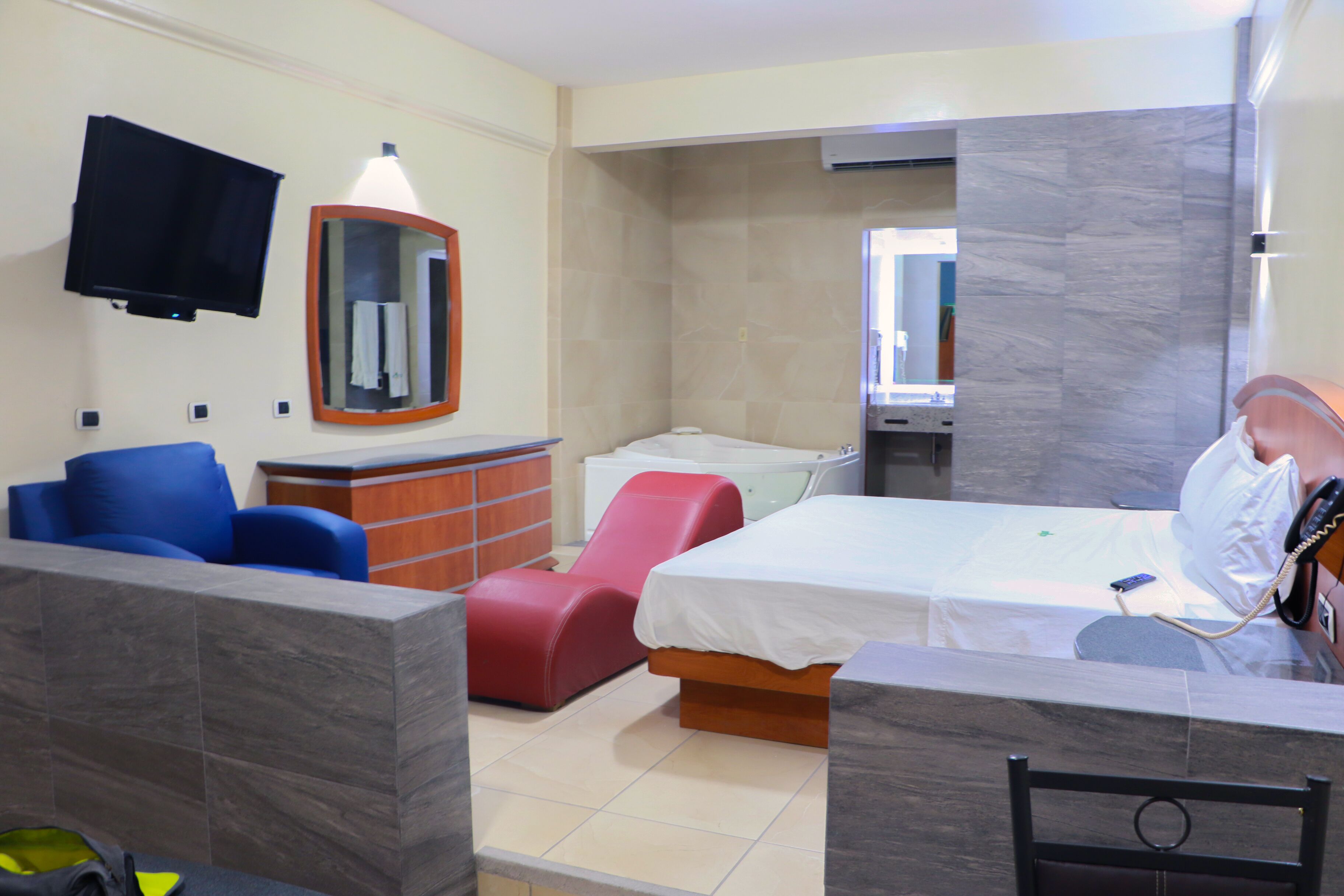 Een hotelkamer met een bed, een bureau, een stoel, een televisie, een spiegel en een rode massagestoel.
