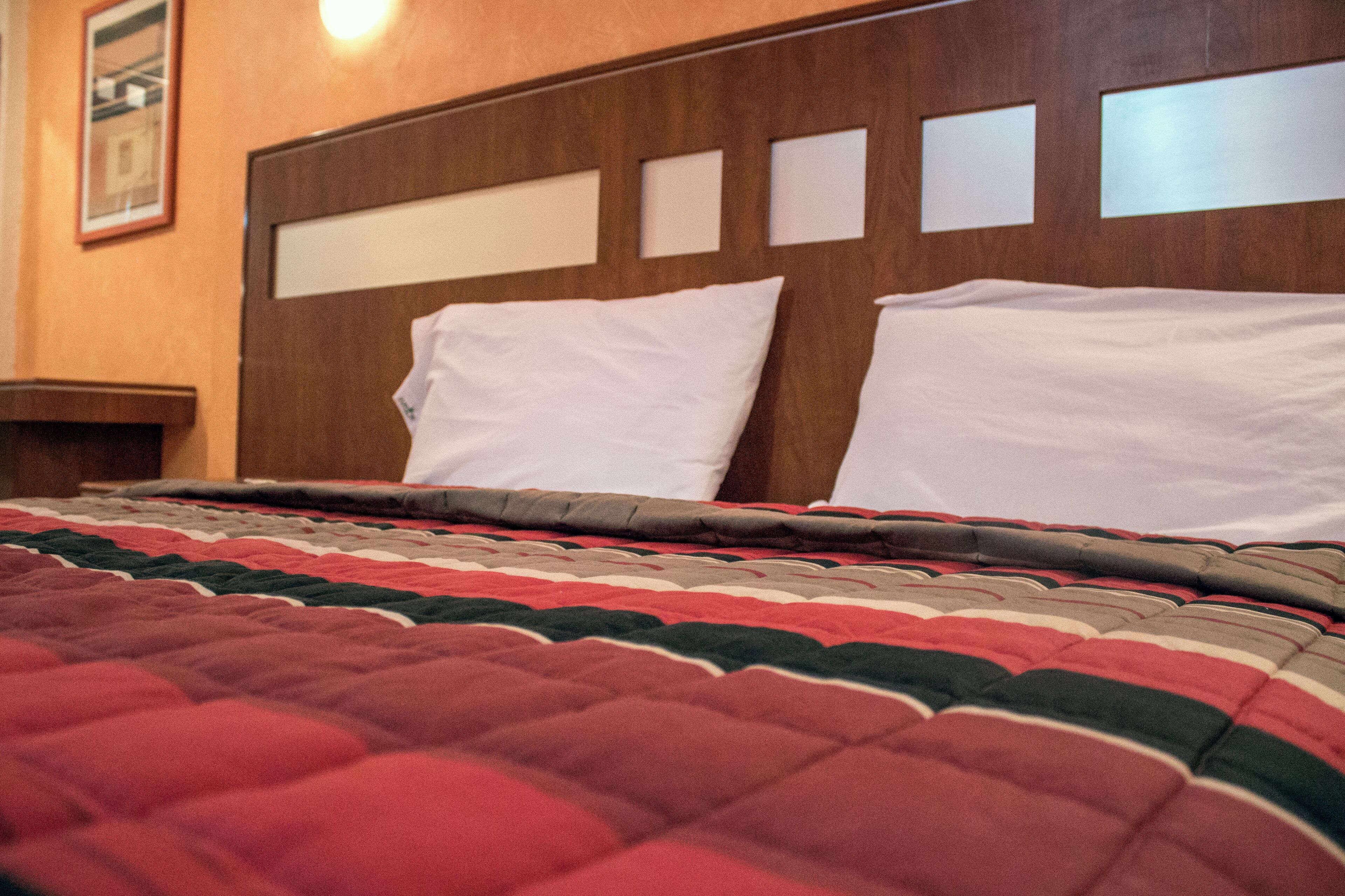 A hotel room with a wooden headboard, a red and green striped bedspread, and white pillows.
