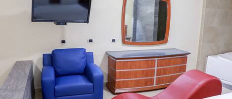Une chambre d’hôtel équipée d’un téléviseur à écran plat, d’une commode en bois, d’un fauteuil bleu, d’une chaise rouge et d’un lit.