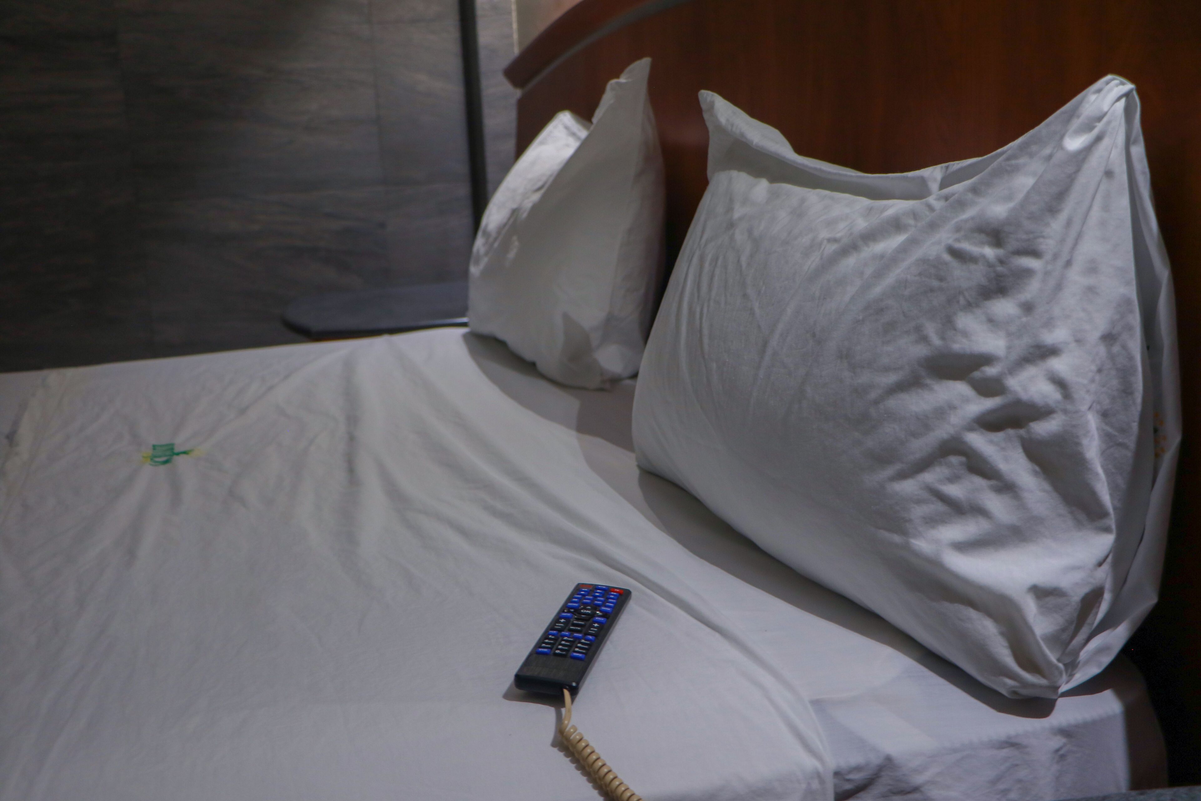 A bed with white bedding, a remote control, and pillows.