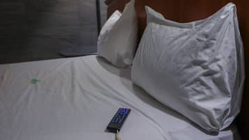A bed with white bedding, a remote control, and pillows.