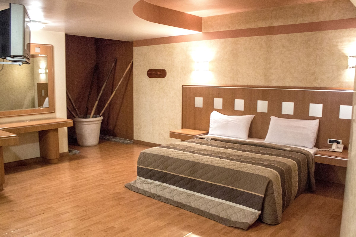 A hotel room with a wooden bed, bedside table, and a large mirror.