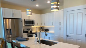 Une cuisine moderne avec des meubles blancs, des appareils en acier inoxydable et un îlot central doté de tabourets de bar.