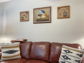 A brown leather sofa with patterned cushions and three framed artworks on the wall.