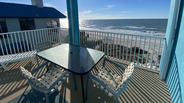 A balcony with a table and chairs, overlooking the ocean.
