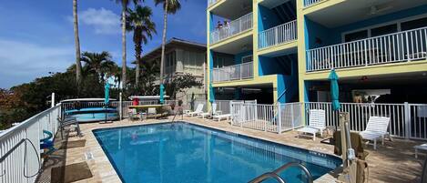 A swimming pool with a metal ladder, surrounded by a white fence and lounge chairs.