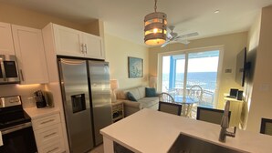 A modern kitchen with stainless steel appliances, a dining area with a view of the ocean, and a ceiling fan.