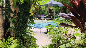 Un espace piscine agrémenté d’un transat et d’un parasol, le tout entouré d’une végétation luxuriante.
