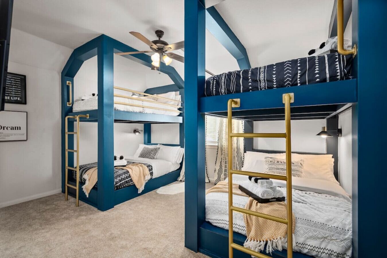 A room with two bunk beds, each with a ladder, a ceiling fan, and a framed inspirational quote on the wall.