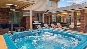 Un patio trasero con jacuzzi, sillas de descanso, una parrilla y un porche cubierto.