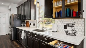 Una cocina moderna con armarios oscuros, un refrigerador de acero inoxidable, una encimera blanca y una ventana con persianas.