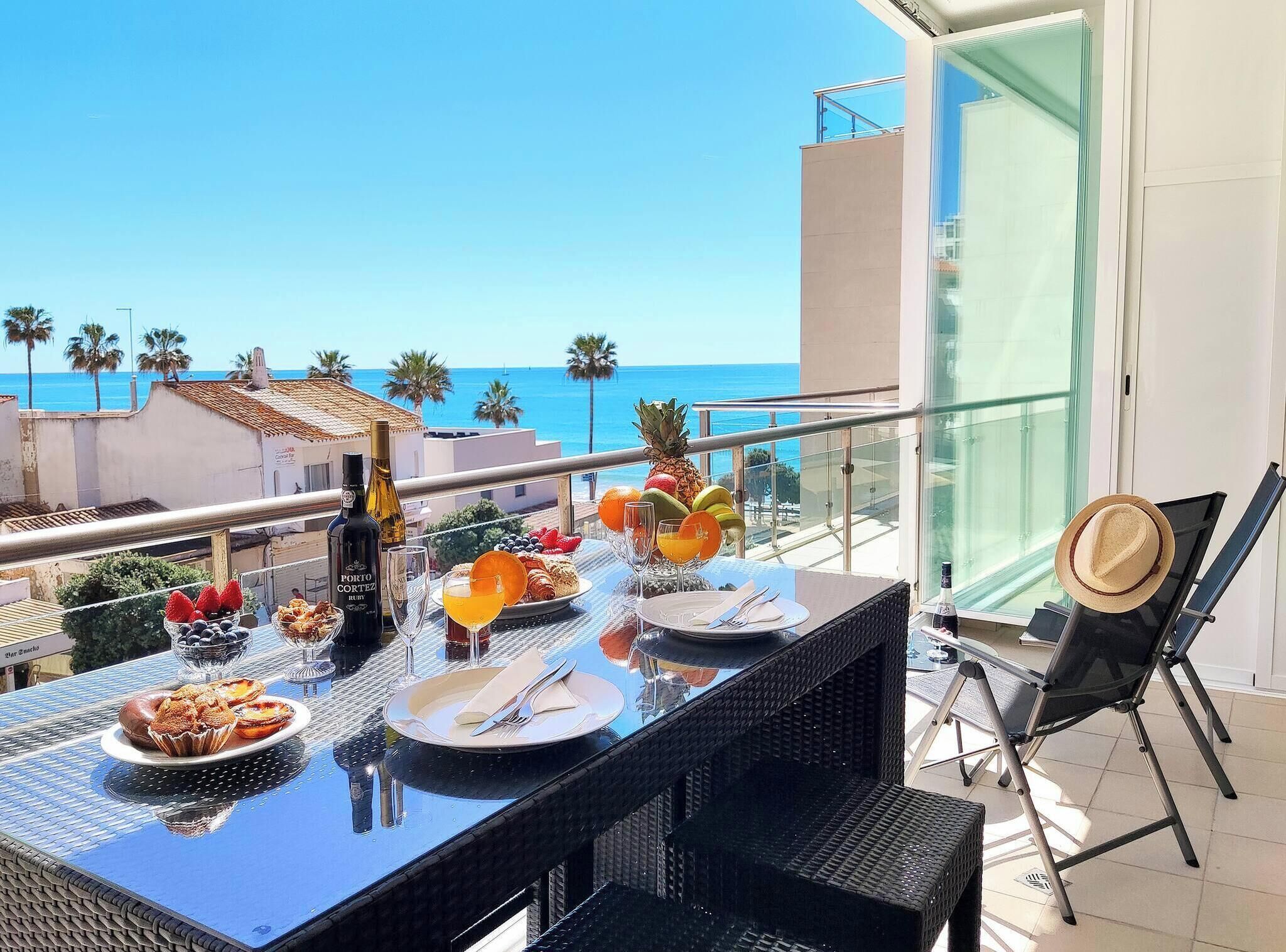 Una mesa de comedor dispuesta con comida y bebidas en un balcón con vistas al mar.