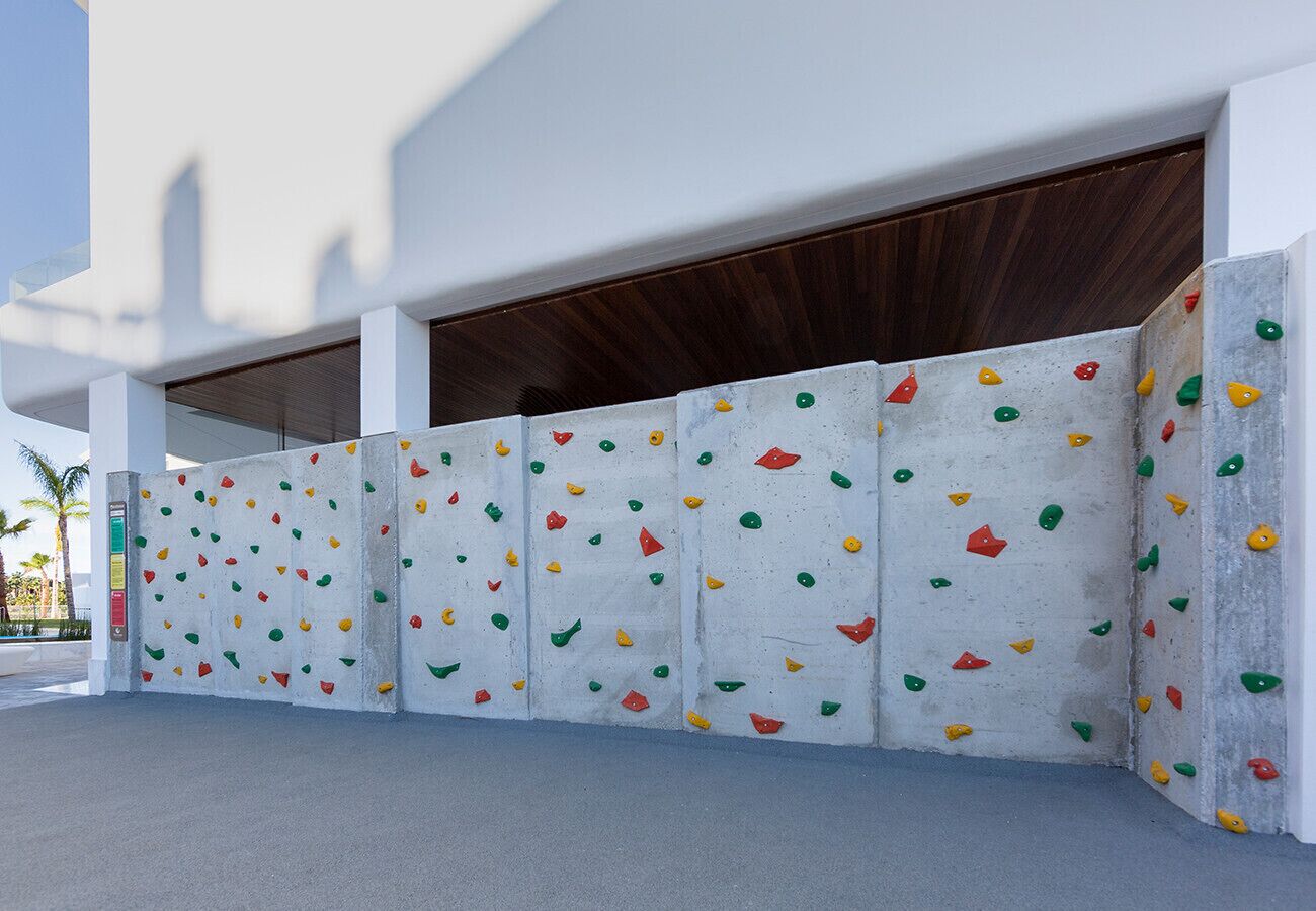 A modern building with a white exterior and a concrete wall with colorful climbing holds.