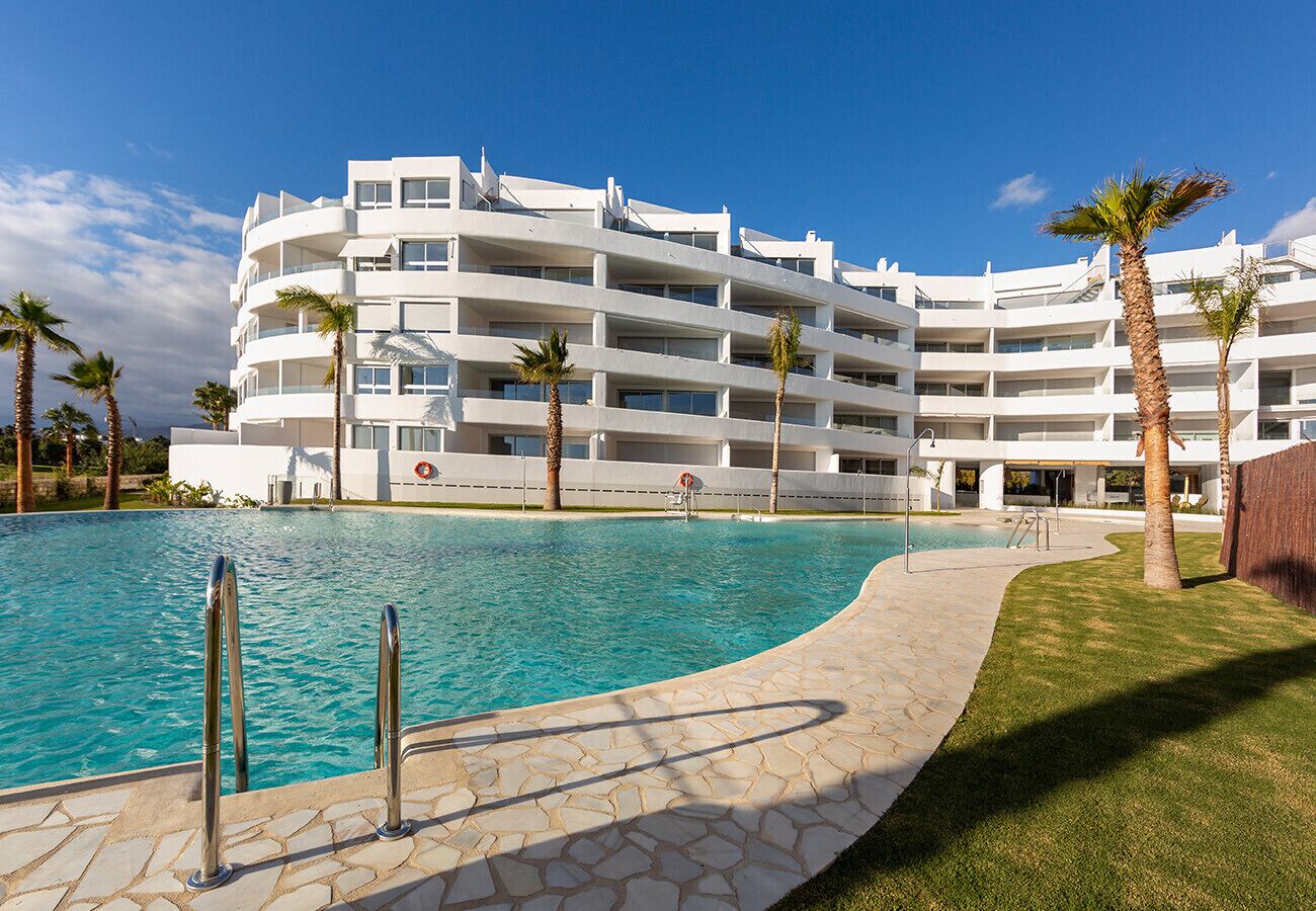 A modern hotel with a pool, palm trees, and a clear blue sky.