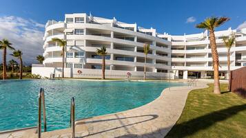 A modern hotel with a pool, palm trees, and a clear blue sky.