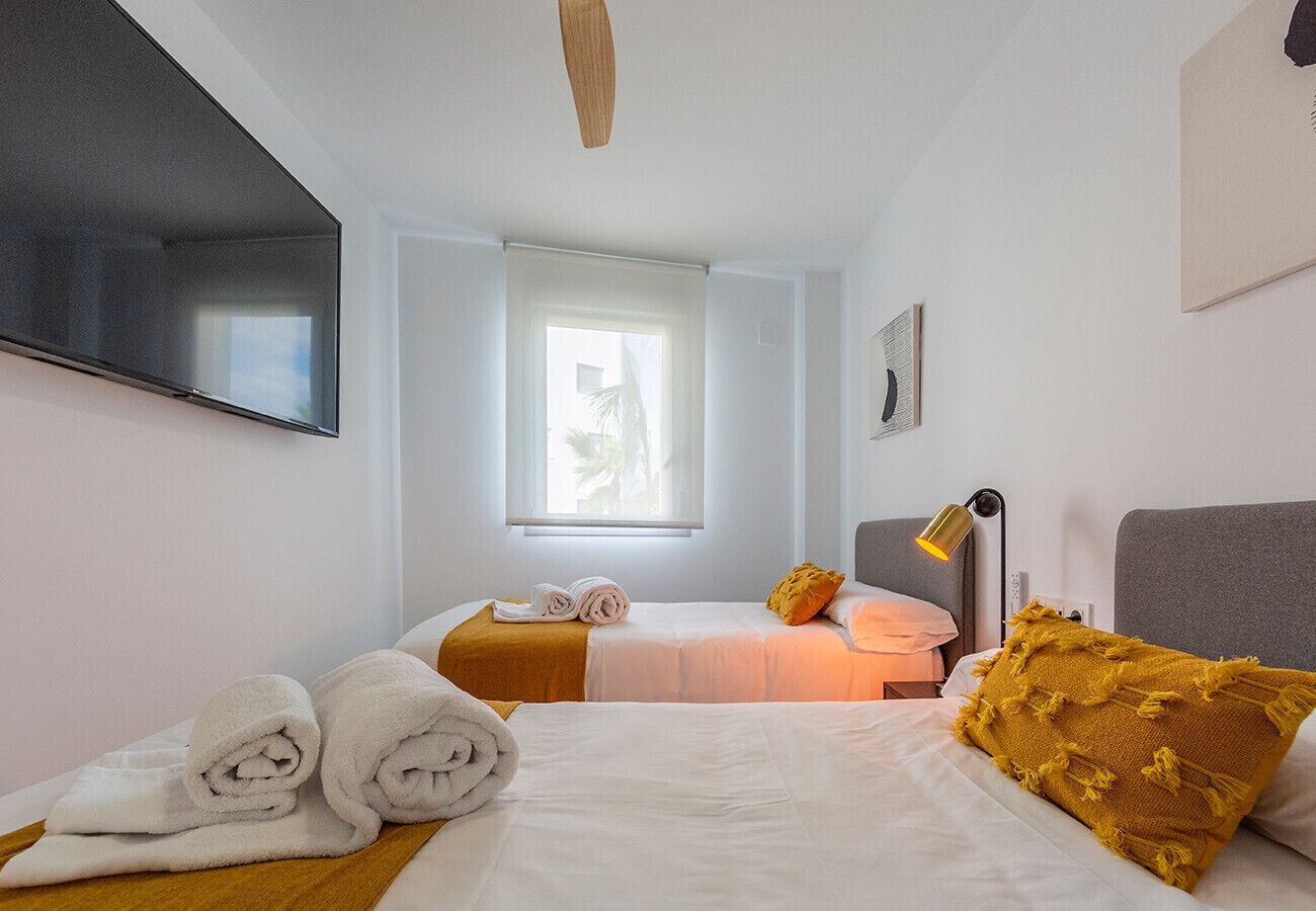 Ett hotellrum med två sängar, en platt-TV som är monterad på väggen, ett fönster med gardiner och en sänglampa.