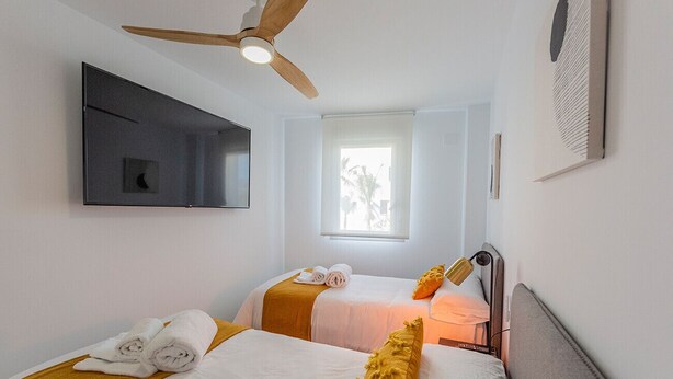 A hotel room with two beds, a ceiling fan, a TV mounted on the wall, and a window with a view of palm trees. - Ref. 346637 (Motril)
