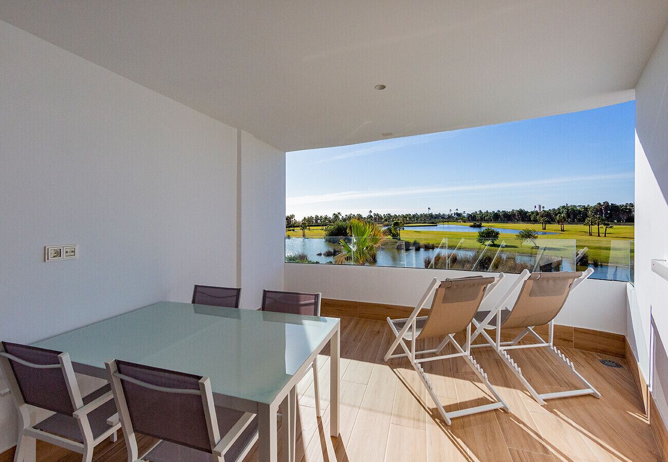 Un comedor moderno con una mesa y sillas de vidrio, vista a un lago y follaje, y piso de madera.