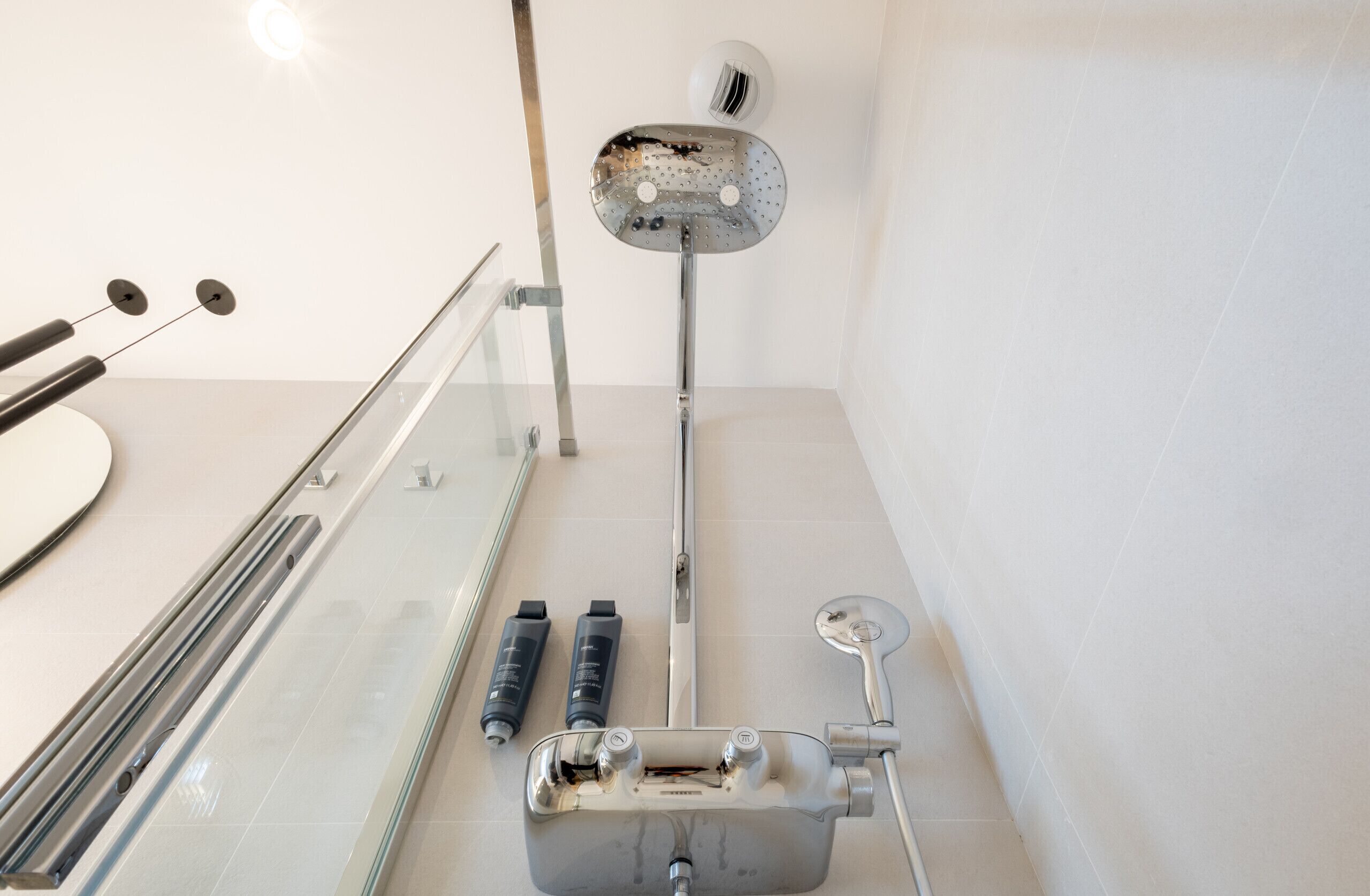 Une salle de bain avec une douche à parois de verre, un pommeau de douche à main et deux bouteilles de shampoing.