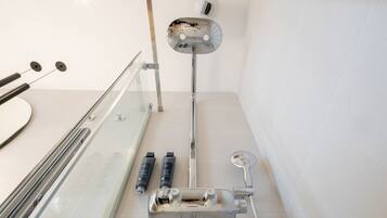 Une salle de bain avec une douche à parois de verre, un pommeau de douche à main et deux bouteilles de shampoing.