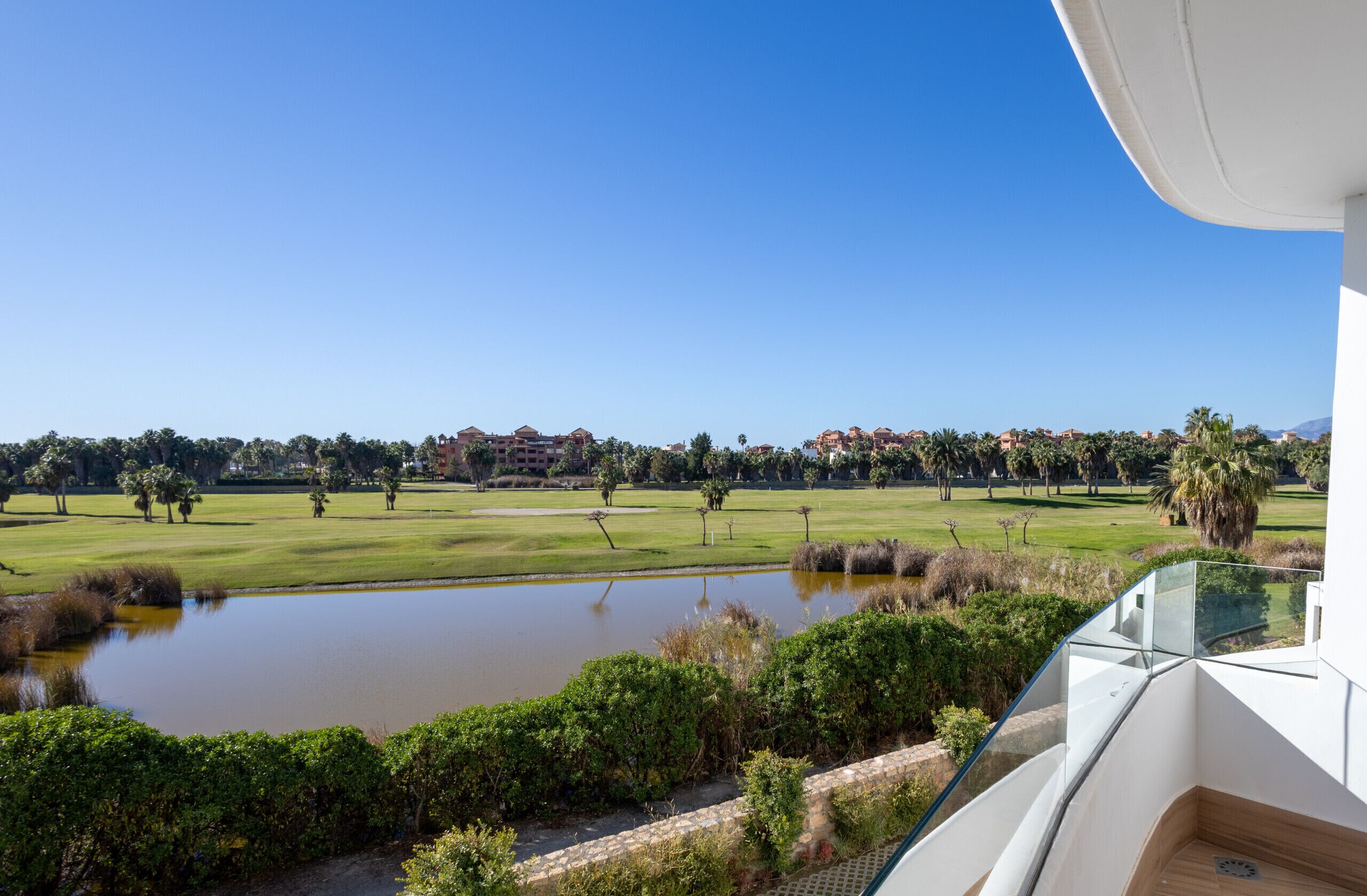 Uitzicht op een golfbaan met een vijver en een gebouw op de achtergrond.