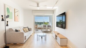 Un soggiorno moderno con divano, tavolino, televisore a parete e un balcone con zona pranzo.