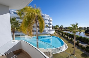 A modern hotel with a pool, palm trees, and a view of a lake.