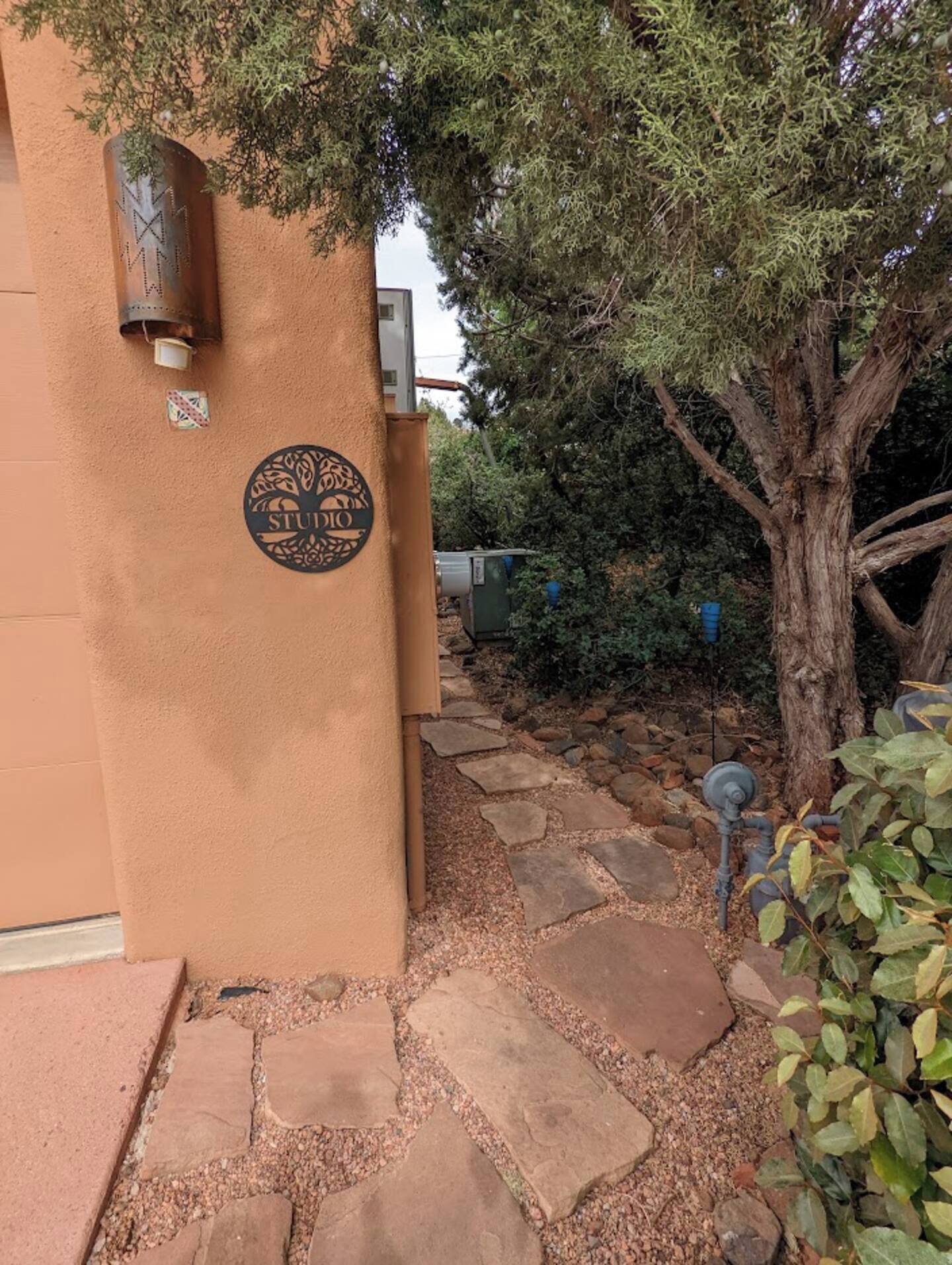 Un bâtiment à l’extérieur recouvert d’enduit, avec un chemin en pierre et un arbre.