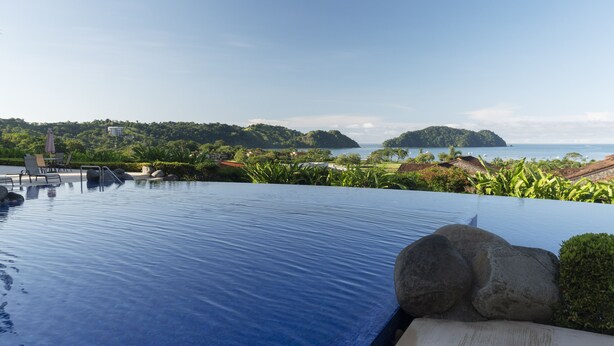 Ein Fernblick von einem Infinity-Pool auf eine tropische Insel und das Meer.