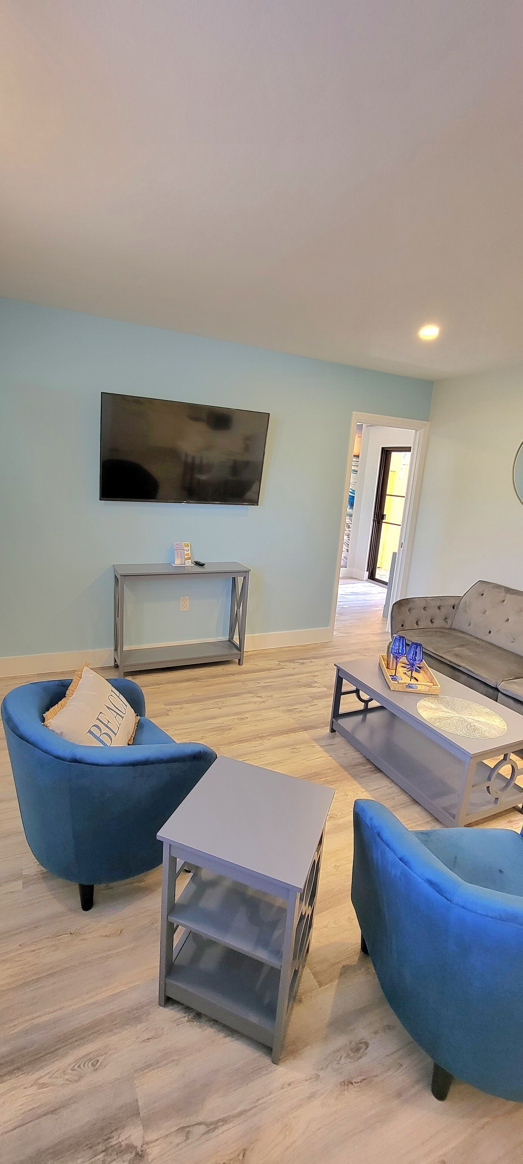 Una sala de estar moderna con un sofá azul, una mesa de centro gris y un televisor montado en la pared.