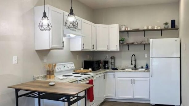 Une cuisine moderne avec des meubles blancs, un îlot central en bois doté de tabourets, une cuisinière et un réfrigérateur.