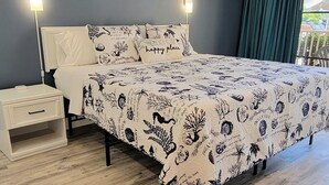 Une chambre à coucher comprenant un lit, des tables de chevet, une commode, un climatiseur fixé au mur et une fenêtre avec des rideaux.