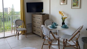 Un balcon avec des fauteuils en osier, une petite table avec des assiettes bleues, un téléviseur et des œuvres d’art accrochées au mur.