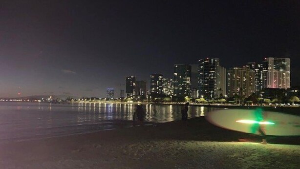 Une vue nocturne d’une ville, avec des bâtiments illuminés et une promenade au bord de l’eau paisible.