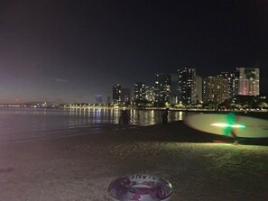 Un paisaje urbano nocturno con edificios iluminados y un frente marítimo tranquilo.