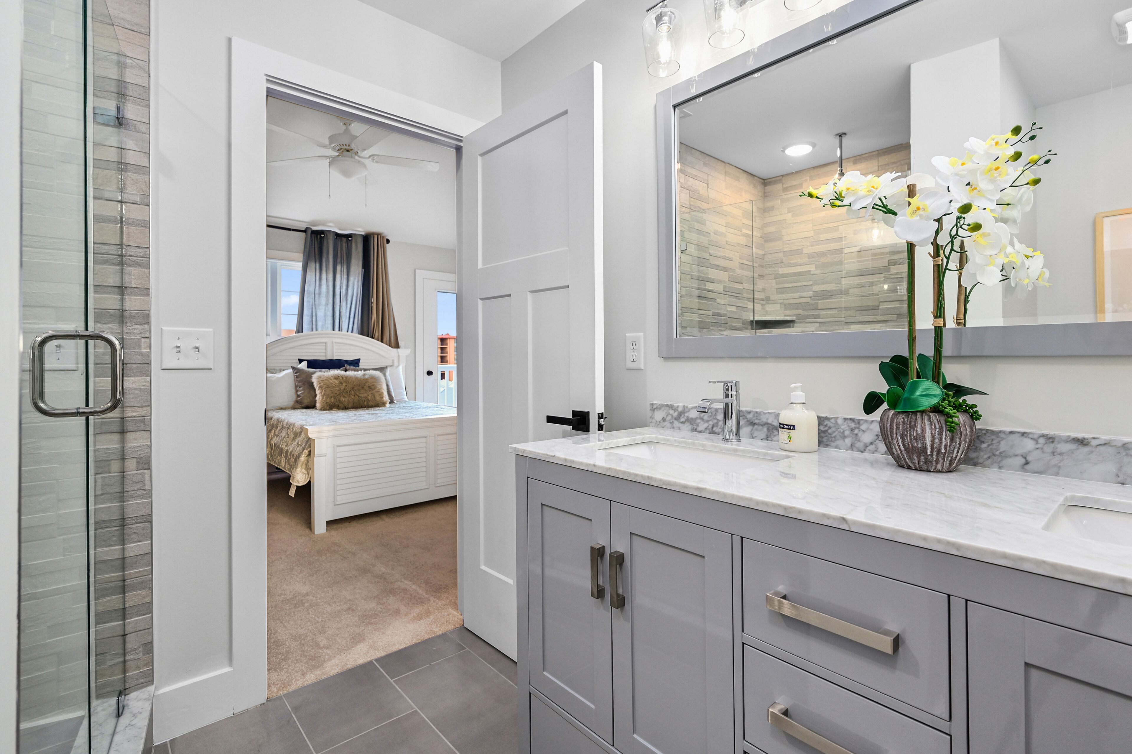 Une salle de bain moderne avec un grand miroir, un comptoir en marbre et une orchidée en pot.