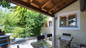 An outdoor patio with a glass table and chairs, surrounded by greenery and a stone pathway.